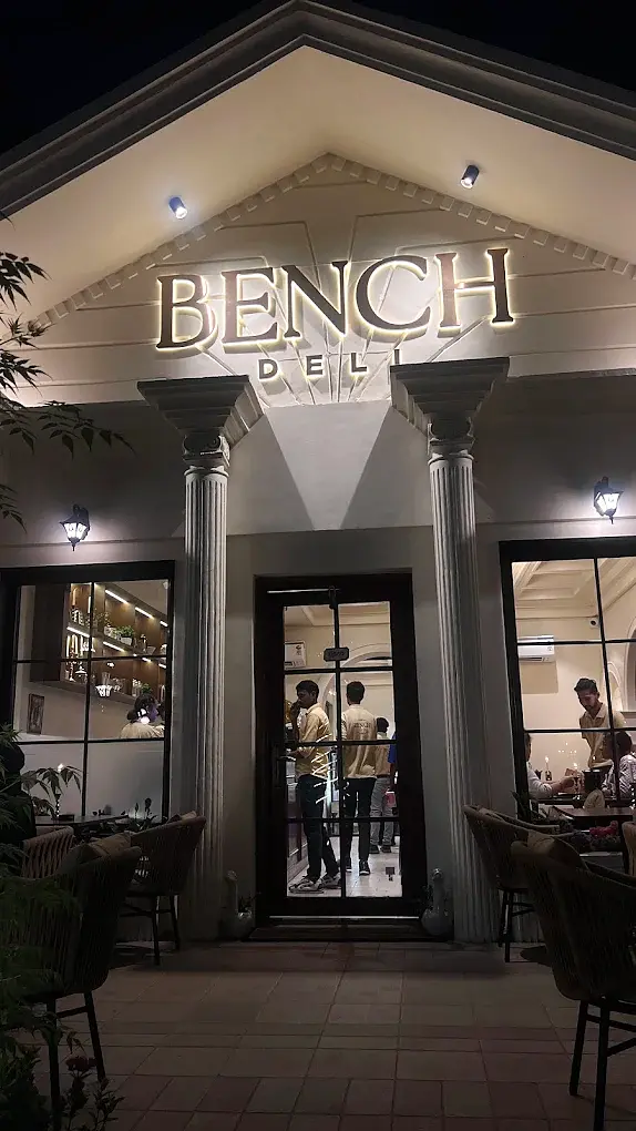 The lit portico of Bench Deli at night, gold BENCH DELI lettering above four columns