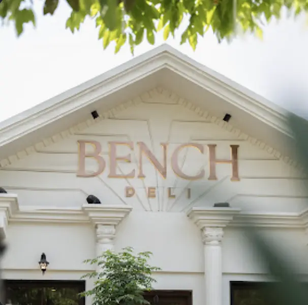 The white pediment of Bench Deli in daylight, gold lettering framed by leaves