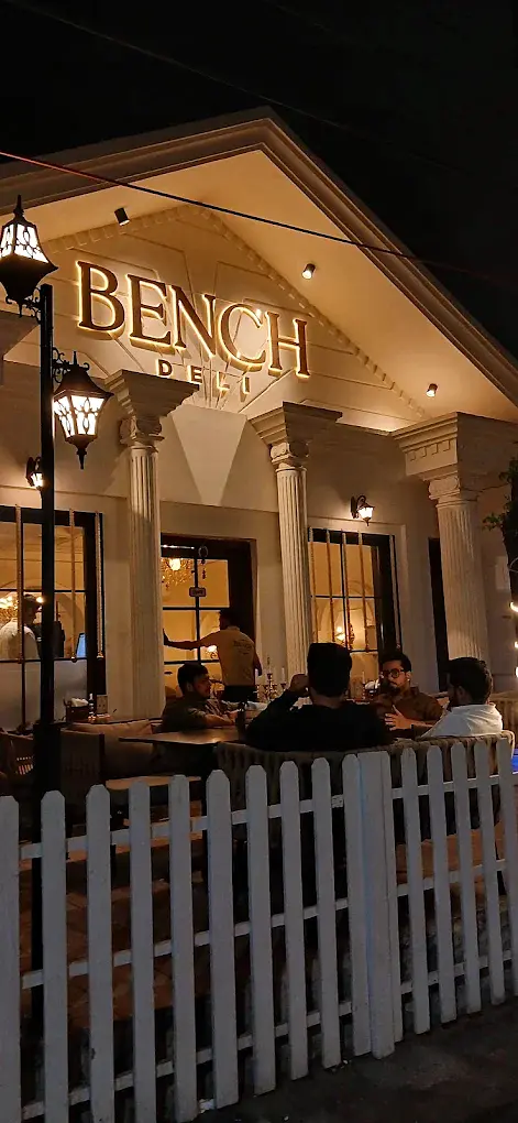 Guests at the outdoor tables under the lit portico at Bench Deli in the evening