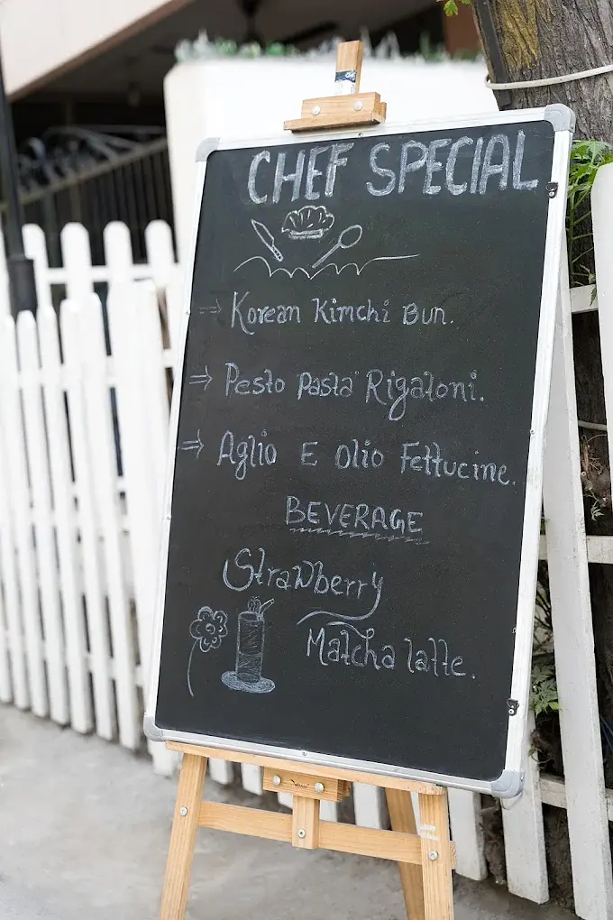 A chalkboard by the gate listing the chef special: Korean kimchi bun, pesto pasta rigatoni, aglio e olio fettucine and a strawberry matcha latte