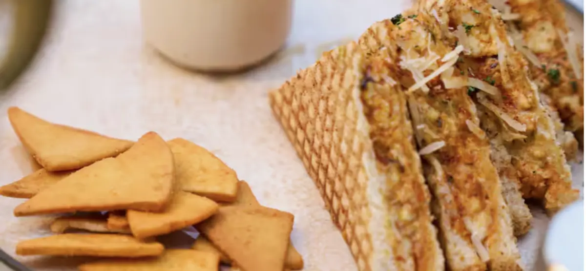 A grilled sandwich cut into fingers, served with pita chips and a coffee