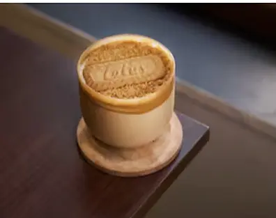 A Biscoff-dusted latte in a ceramic cup on a wooden table